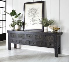 there is a black dresser with two plants on it and a framed picture in the corner