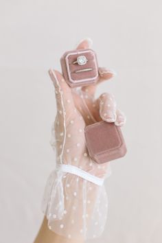 a woman's hand holding a tiny ring with a diamond on it and a small box in the middle