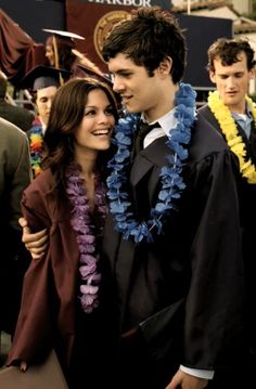 a man and woman standing next to each other in front of graduation cap and gown