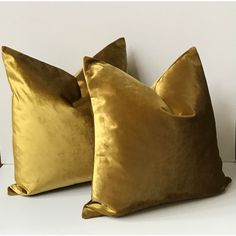 two gold velvet pillows sitting on top of a white table next to a black vase