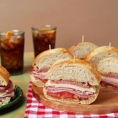 sandwiches with meat and cheese are on a wooden platter next to two glasses of soda