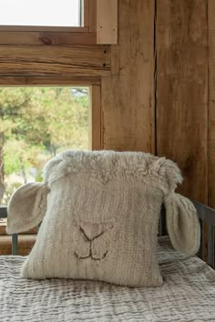 a sheep pillow sitting on top of a bed next to a wooden wall and window