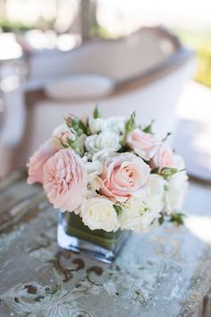 a vase filled with pink and white flowers on top of a table next to a chair