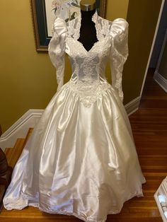 a white wedding dress on display in front of a framed photo and wooden flooring