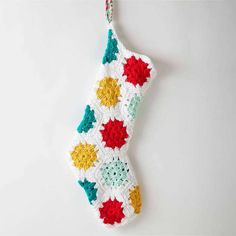 a crocheted christmas ornament hanging on a white wall with red, yellow and green stars