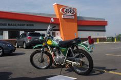 a green motorcycle parked in front of a building next to a parking lot filled with cars