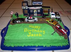 a birthday cake with cars and people on the road in front of a police station