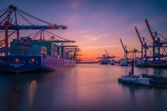 there are many cranes that are in the harbor at sunset or dawn, and one is on the other side of the dock