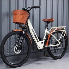 an orange and white bicycle parked next to a metal wall with a basket on the front