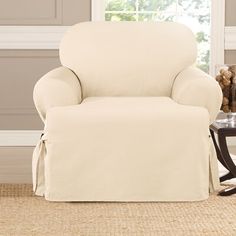 a living room with a chair covered in a white slipcover next to a window