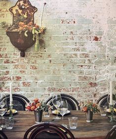 a wooden table topped with lots of chairs next to a brick wall covered in flowers