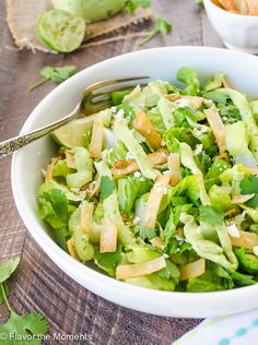 a white bowl filled with lettuce and topped with dressing next to a fork