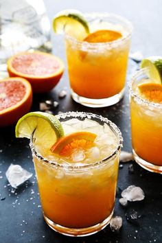 three glasses filled with orange juice and garnished with limes on the side