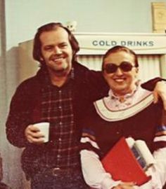 two people standing next to each other in front of a building holding coffee cups and books