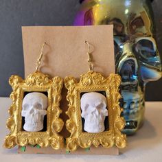 a pair of skull head earrings sitting on top of a table next to a gold frame