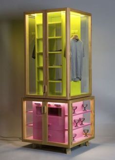 a pink and yellow display case with clothes on it's sides, in front of a white wall