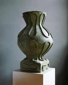 a green vase sitting on top of a white pedestal