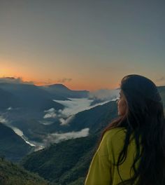 a woman standing on top of a mountain looking out at the clouds in the valley