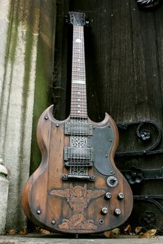 an old guitar sitting on the ground in front of a wooden door with a cross painted on it