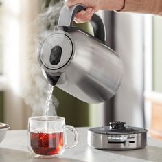 a person pouring tea into a glass mug