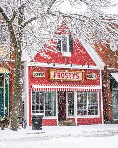 a red and white striped store with snow falling on it's roof, next to a tree