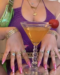 a woman holding a martini glass with pink and green nail polishes on her hands