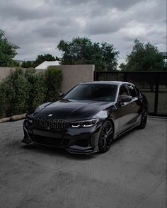 a black bmw car parked in front of a fence and bushes on a cloudy day