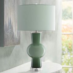 a green lamp sitting on top of a white table next to a wall mounted mirror