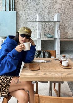 a woman sitting at a table with a coffee cup in her hand and wearing leopard print shorts