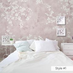 a white bed sitting next to a pink wall with flowers on it and two pictures above the bed