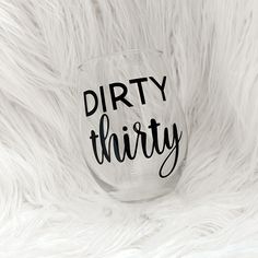 a wine glass that says dirty thirty sitting on top of some white fluffy fur with the words dirty thirty written in cursive font