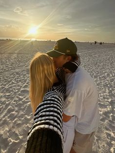 a man and woman kissing on the beach at sunset with people walking in the background