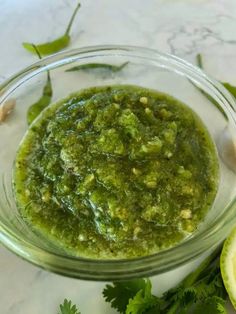 a glass bowl filled with green sauce next to sliced limes and cilantro