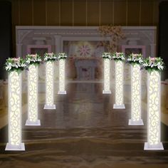 a set of four white columns with flowers on them in the middle of a room