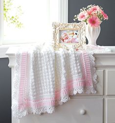 a crocheted baby blanket sitting on top of a dresser next to a vase with flowers