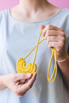 a woman holding a yellow piece of yarn in one hand and a string in the other