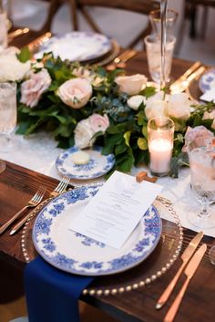 the table is set with blue and white plates, silverware, candles and flowers