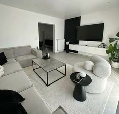 a living room with white couches and black tables in the center, television mounted on the wall