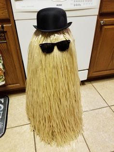 a hat and sunglasses are on top of a fake grass man's head in the kitchen