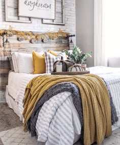 a bed with yellow and gray blankets on it in front of a white brick wall