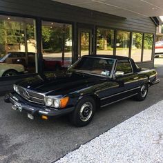 a black mercedes benz parked in front of a car dealership with cars behind it