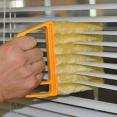 a person is cleaning the blinds with a yellow dust mop and cloth on it