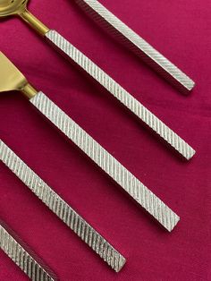 four pieces of silverware on a pink tablecloth with a gold fork and knife