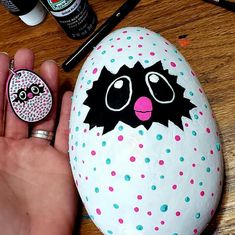 a hand holding a painted rock with an image of a black cat and pink polka dot