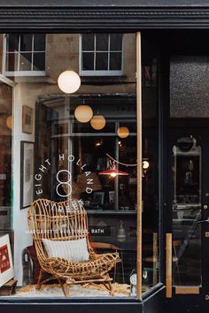 a wicker chair sitting in the window of a store front with lights hanging above it