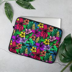 an open laptop computer case with colorful flowers on it and green leaves next to it