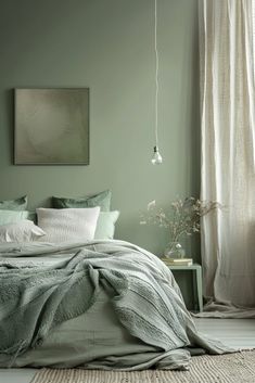 a bedroom with green walls and bedding in the corner, there is a painting on the wall