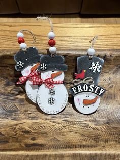 two snowmen wearing hats and scarfs are hanging from hooks on a wooden surface