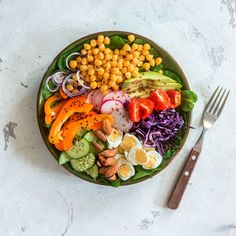 a plate filled with vegetables and chickpeas next to a fork on a table