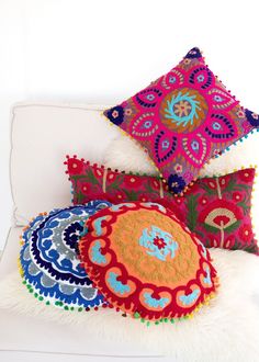 four colorful pillows on a white couch with fluffy fur around the edges and one has an embroidered flower design